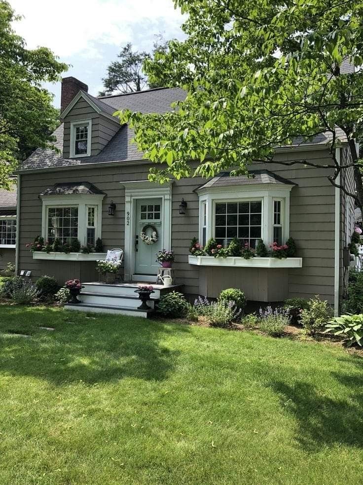 a gray house with white windows and flowers in the window boxes on the front porch