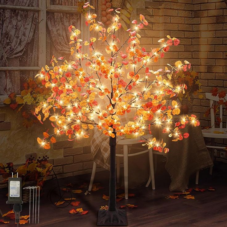 a lighted tree with leaves on it in front of a brick wall and table cloth