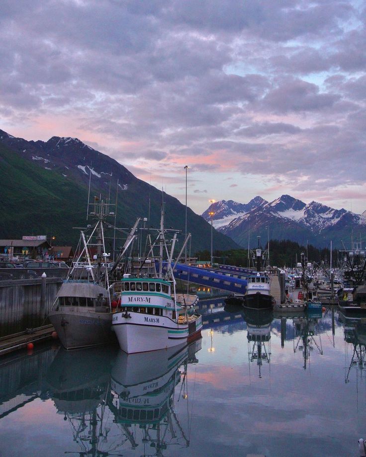 several boats are docked in the water at dusk with mountains in the background and snow - capped peaks