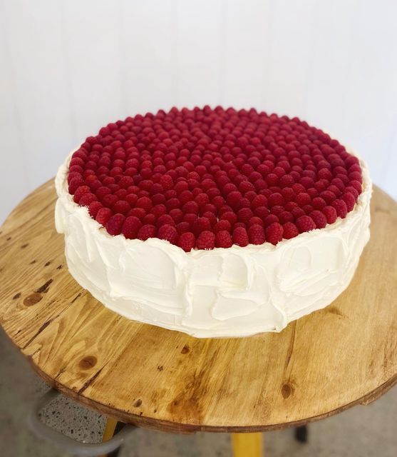 a cake with white frosting and raspberries on top sitting on a wooden table