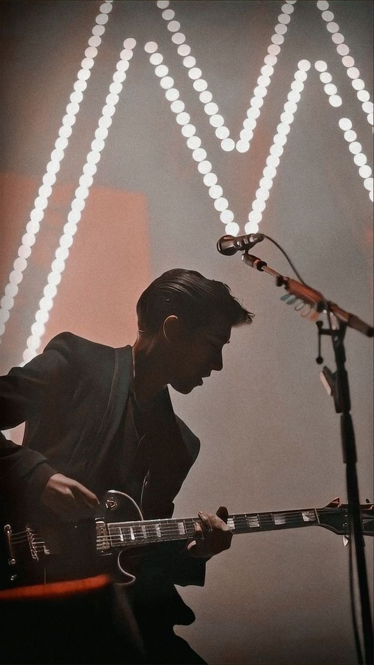 a man playing an electric guitar in front of a microphone and some lights on the wall