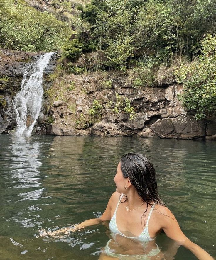 a woman swimming in the water next to a waterfall