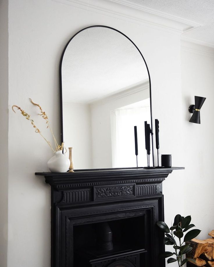 a fireplace with a mirror on top of it next to a potted plant and fire place