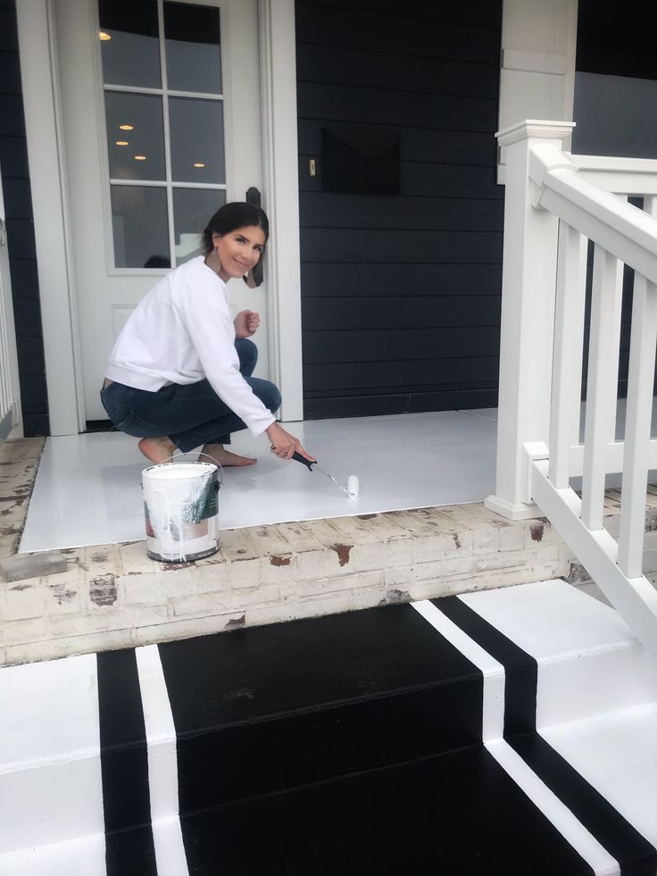 a woman is painting the front steps of a house with black and white stripes on it