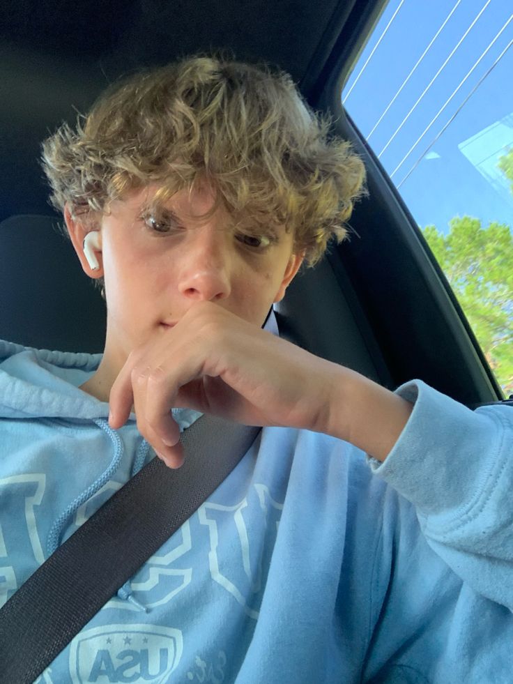 a boy sitting in the back seat of a car with his hand on his chin