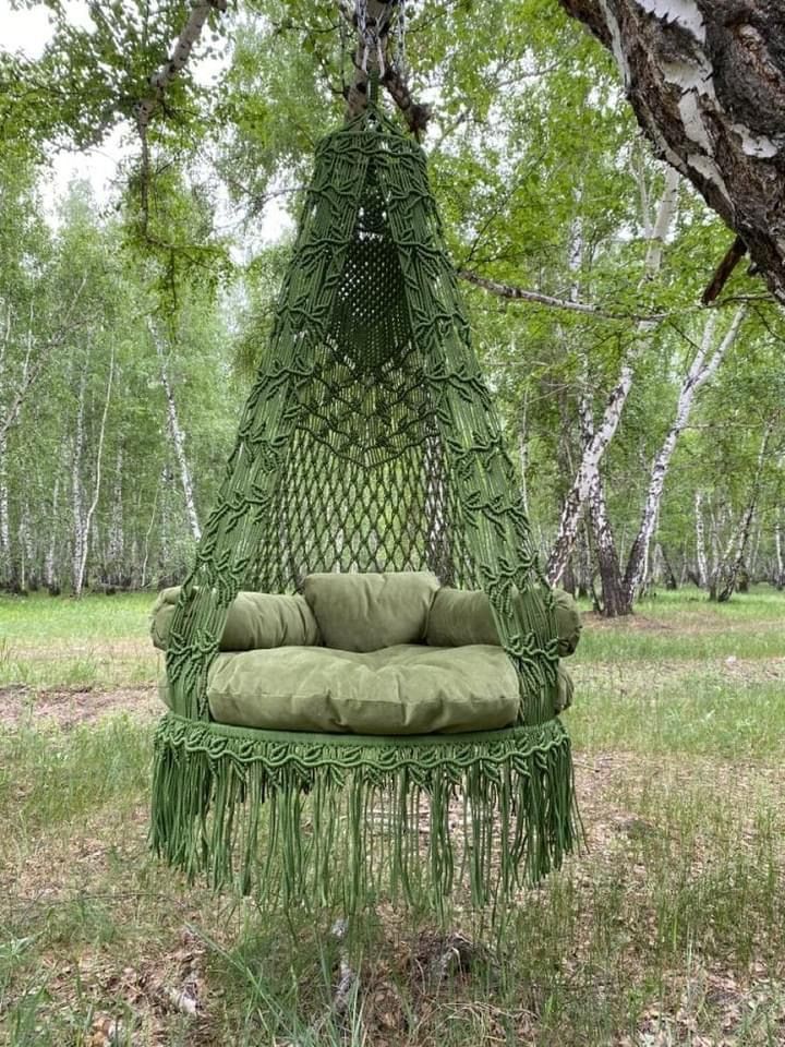 a green hammock hanging from a tree in the woods with pillows on it