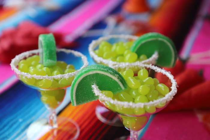 two margaritas with lime slices and candy in them sitting on a colorful table cloth