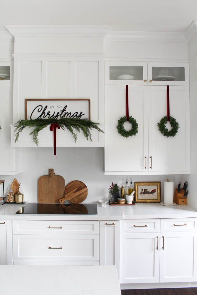 a kitchen decorated for christmas with wreaths on the cabinets and cutting board hanging from the wall