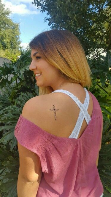 a woman with a cross tattoo on her back, standing in front of some trees