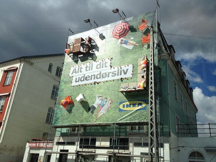 a large billboard on the side of a building with people sitting at tables and umbrellas