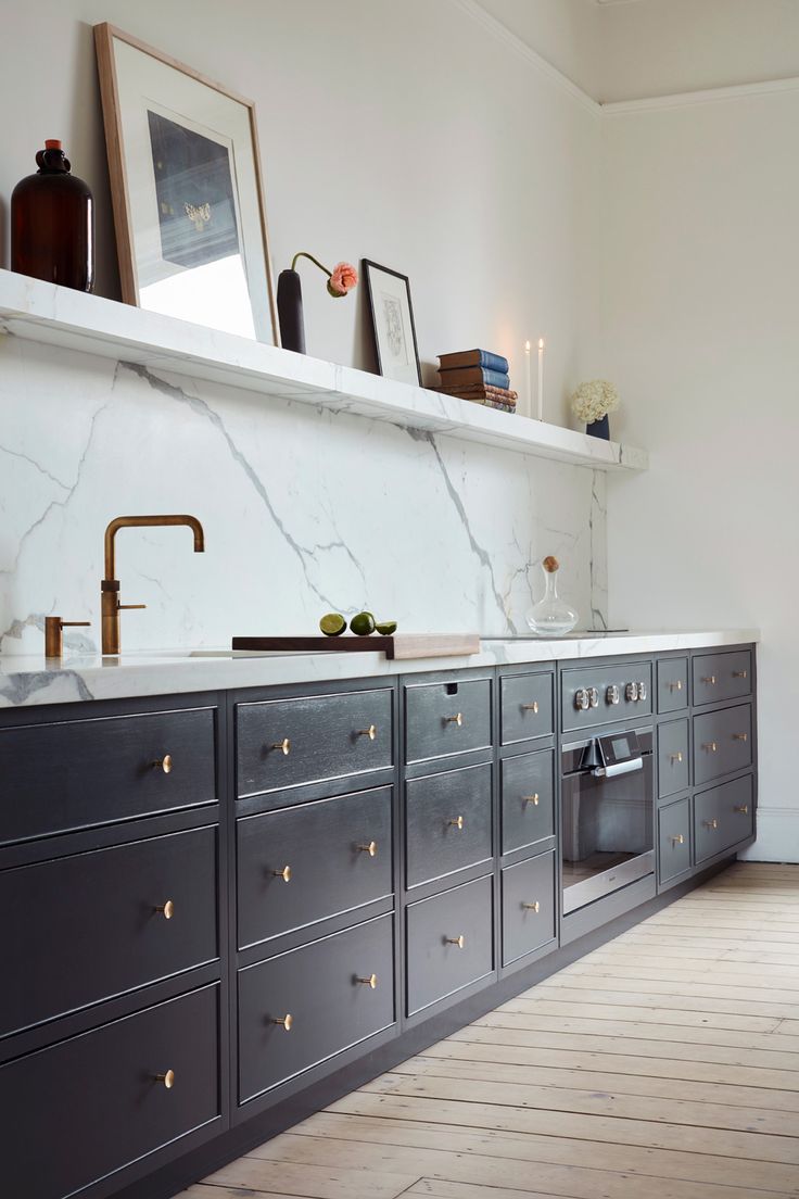 a kitchen with marble counter tops and gray cabinets, gold pulls on the faucet