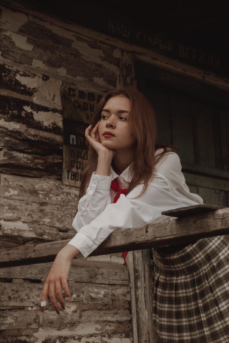 a woman in a skirt leaning against a wooden fence with her hand on her chin