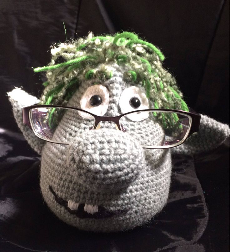 a crocheted stuffed animal wearing glasses on top of a black surface with green hair and eyeglasses