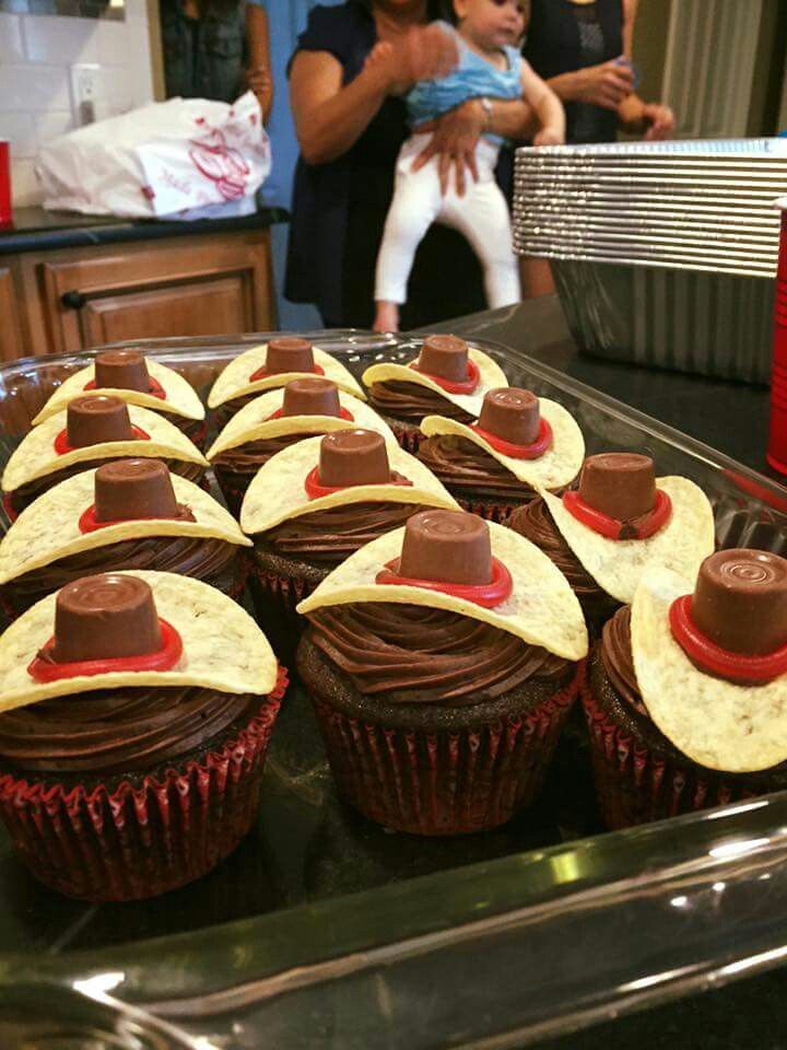 cupcakes with chocolate frosting and hats on them sitting on a baking tray