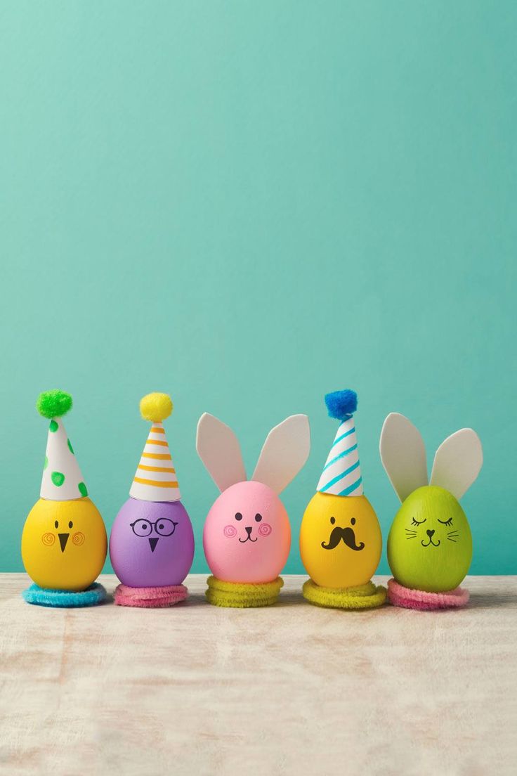 five colorful easter eggs with faces painted on them, lined up against a turquoise background