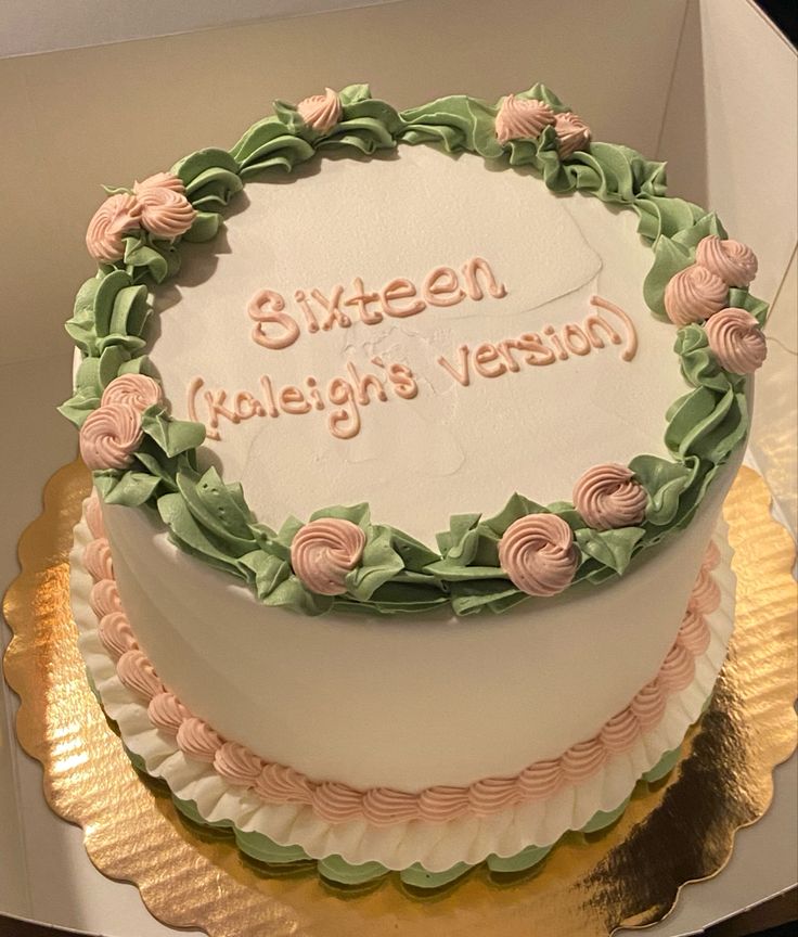 a white cake with pink and green frosting on a gold platter in a box