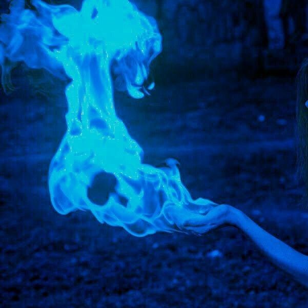 a woman holding a blue lit object in her right hand with fire coming out of it