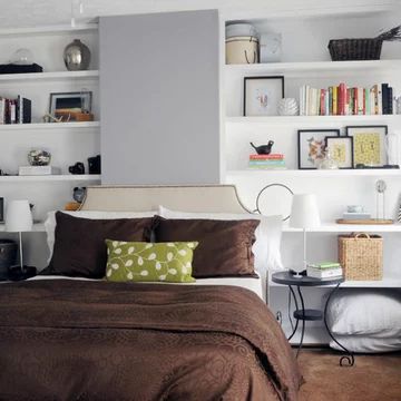 a bed sitting in a bedroom next to a white shelf filled with lots of books