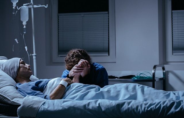 two people laying in a hospital bed with one holding the other's head as they look at each other