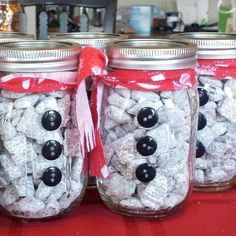 four jars filled with white and black candies sitting on a red tablecloth covered counter