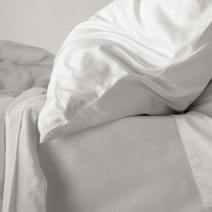 an unmade bed with white sheets and pillow cases on it's side, in black and white