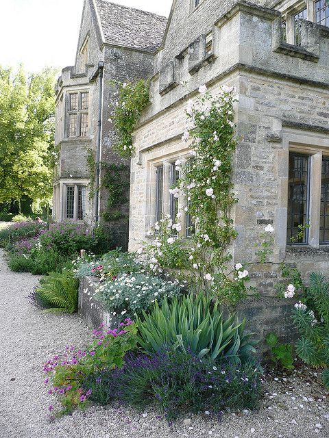 an old stone house with lots of flowers and plants growing out of the front yard