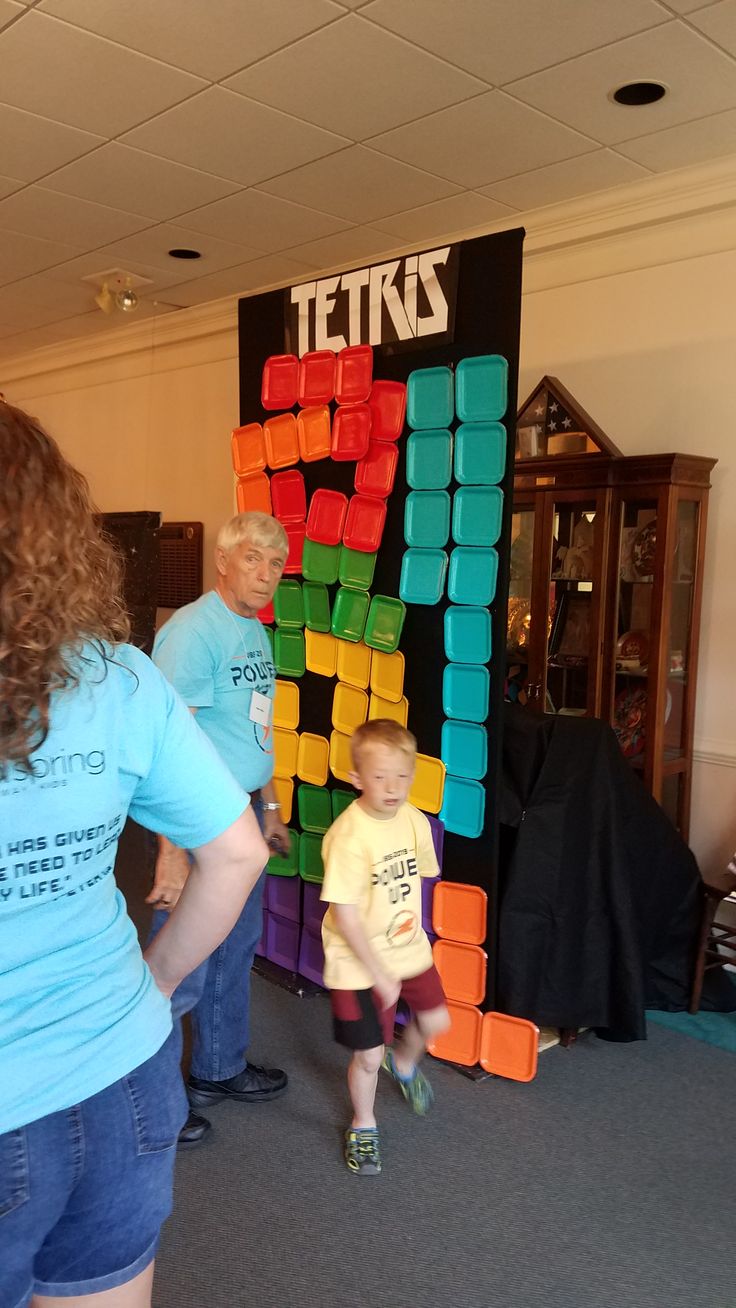 a woman standing next to a child in front of a tetris sign with blocks on it