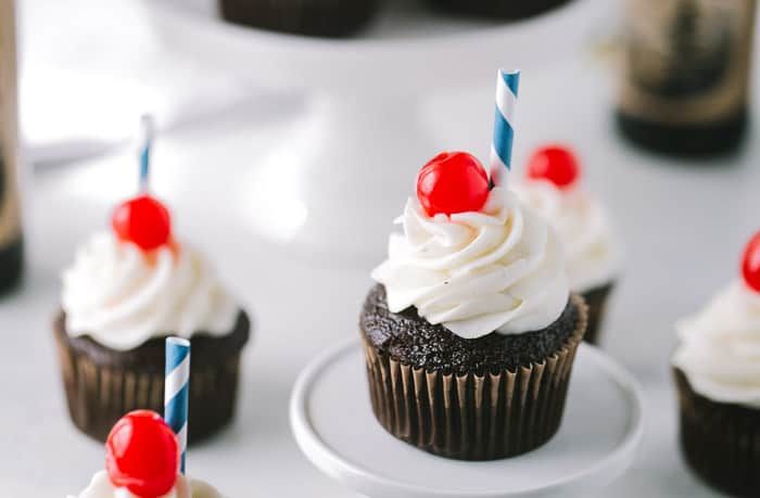 chocolate cupcakes with white frosting and cherries on top, decorated with candles