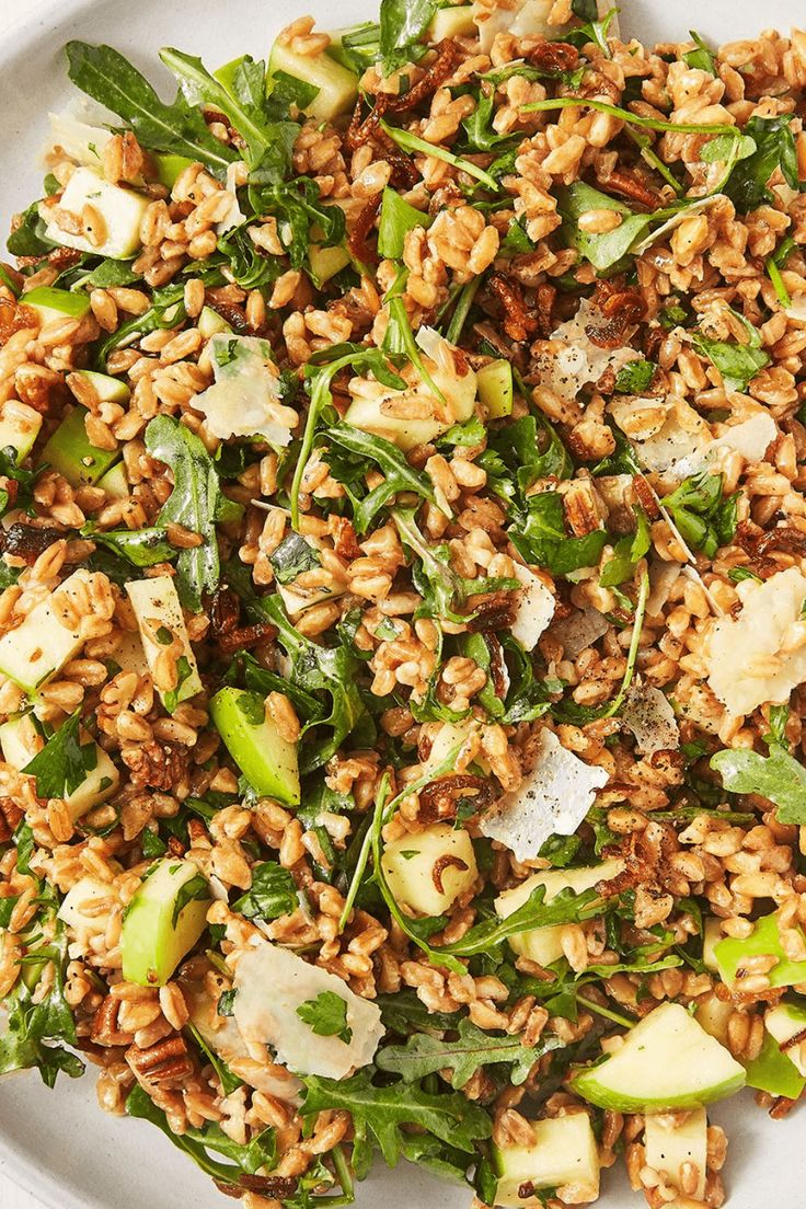 a white plate topped with farro salad on top of a wooden table next to utensils