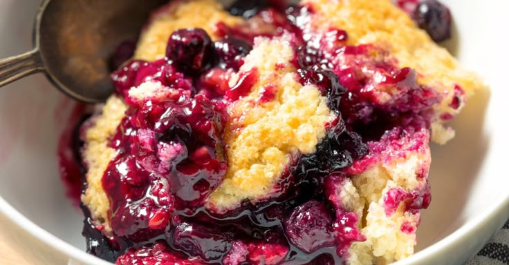 blueberry cobbler in a white bowl with a spoon on the side, ready to be eaten