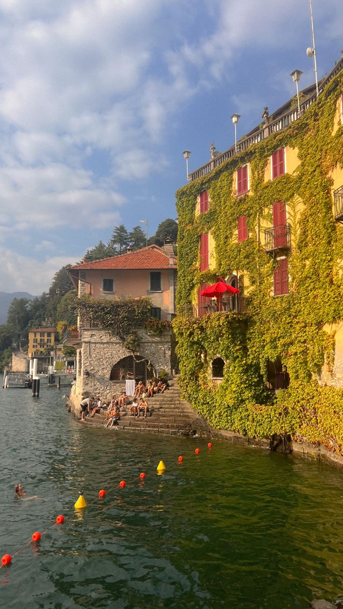 people swimming in the water next to an old building with ivy growing on it's side