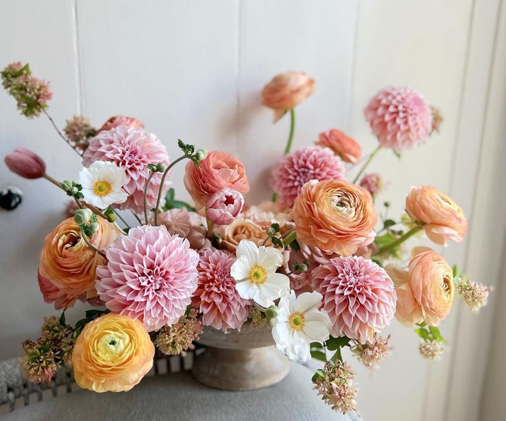 a vase filled with lots of flowers on top of a white table next to a wall