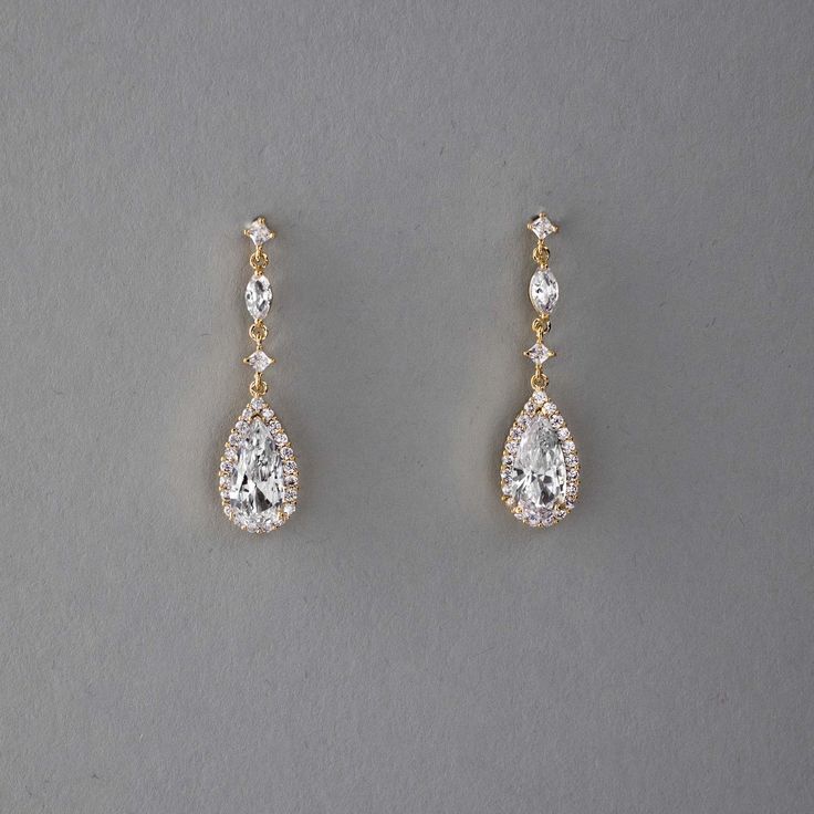 two pairs of diamond earrings on a gray surface with one pair dangling from the side