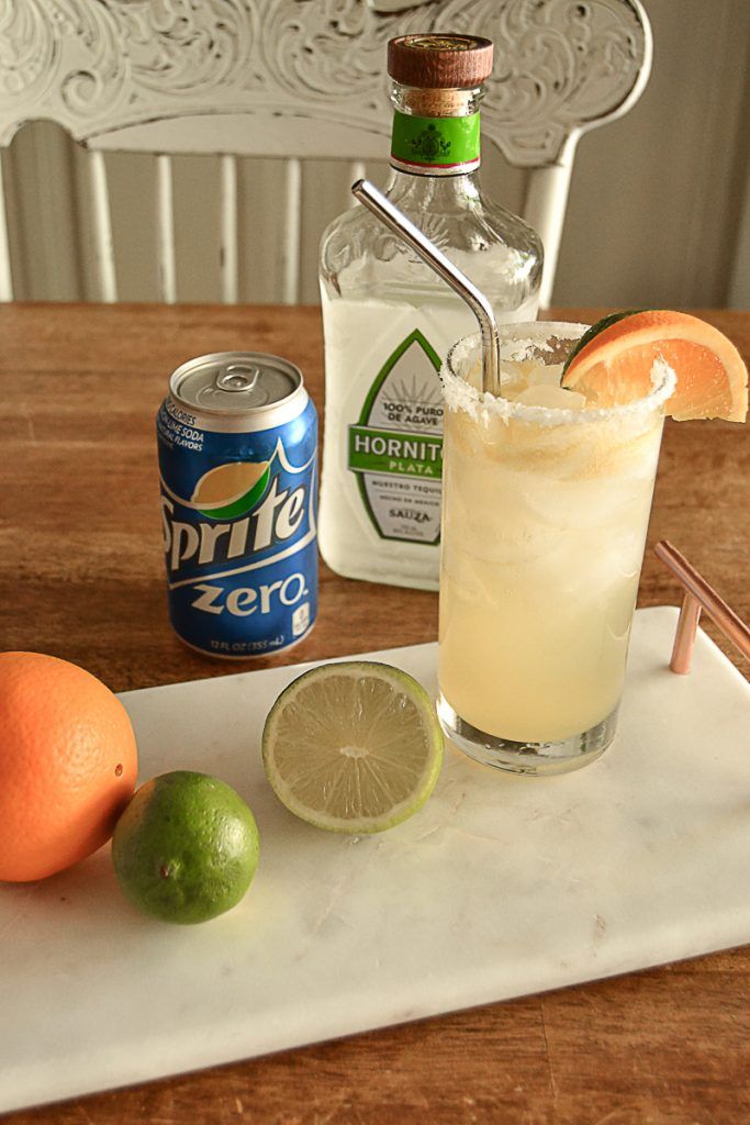 an alcoholic drink on a tray with limes and oranges