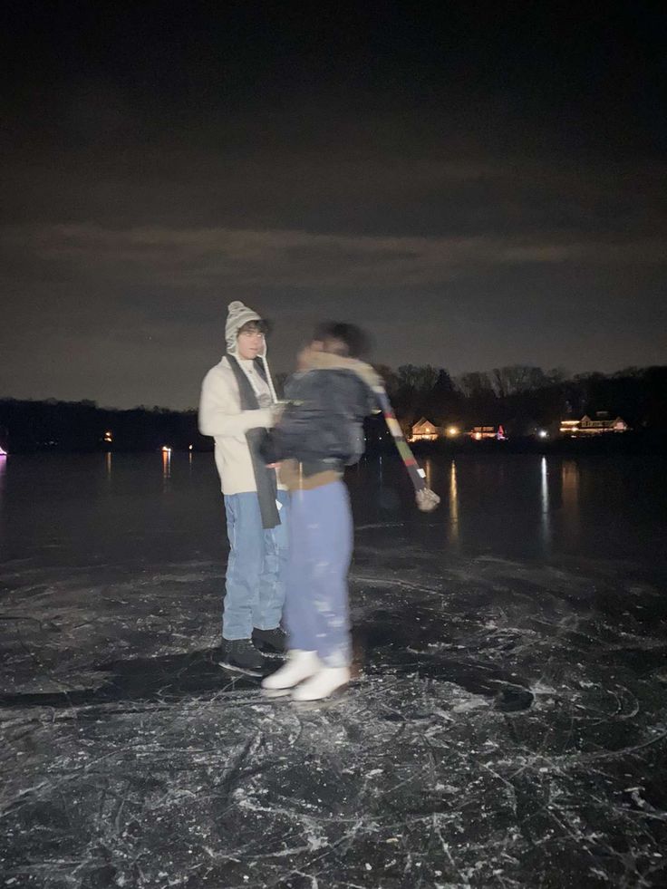 two people are standing on an ice rink at night