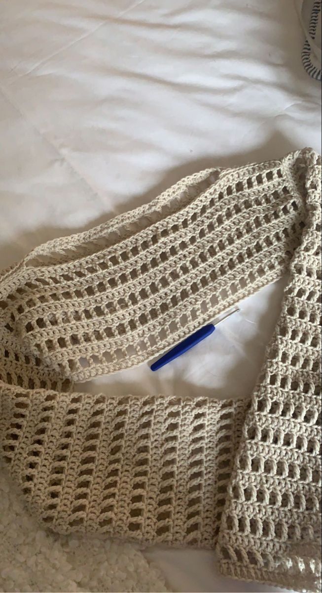 a crocheted neck tie laying on top of a white bed with a blue pen sticking out of it