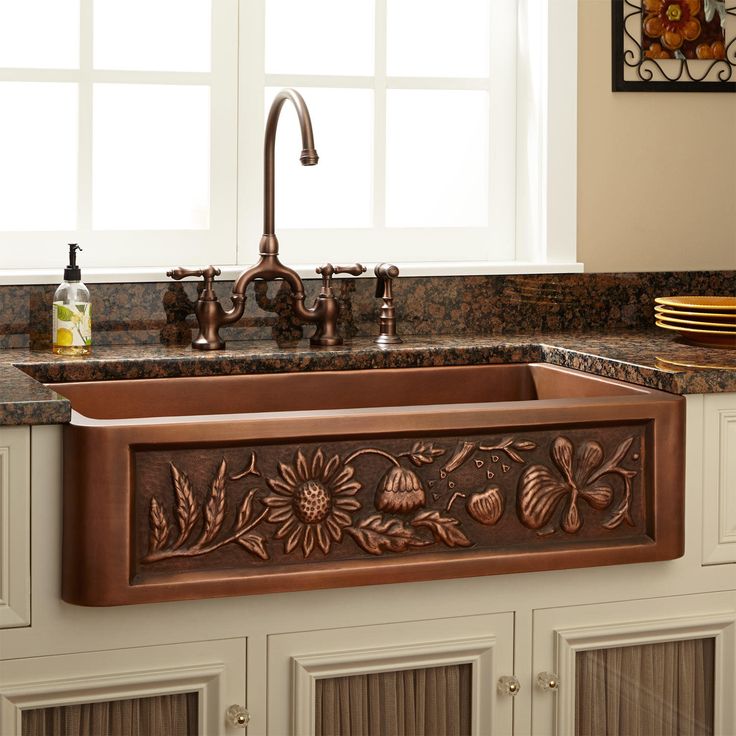 a kitchen sink sitting under a window next to a vase with flowers on top of it