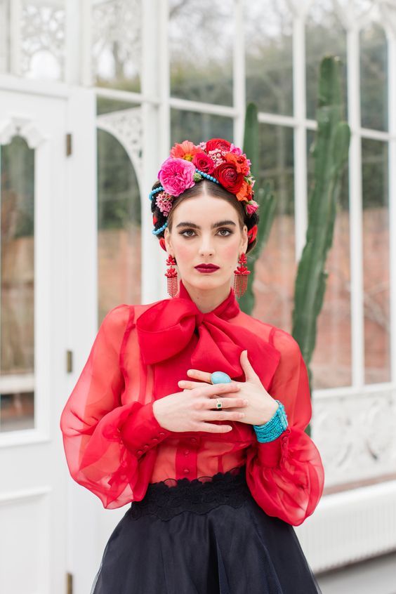 a woman in a red top and black skirt with flowers on her head standing outside