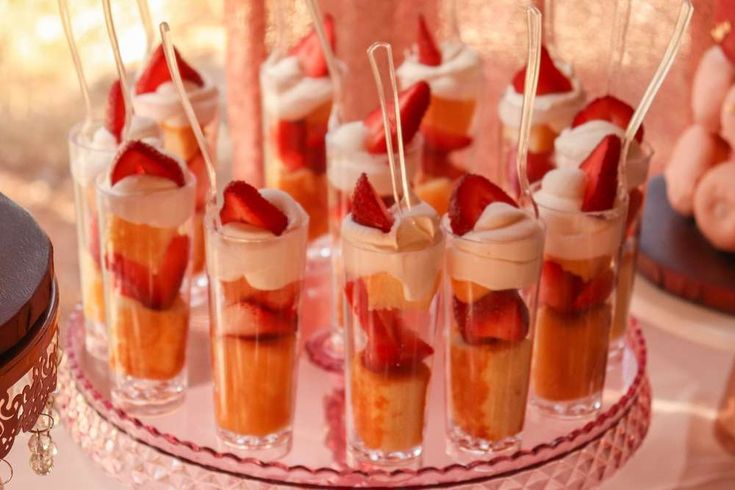 small desserts with strawberries and whipped cream are on a pink plate next to other desserts