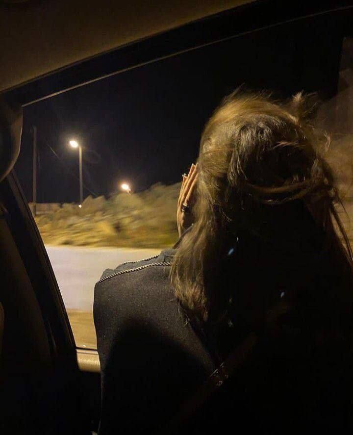 a woman sitting in the passenger seat of a car at night with her hand on her head