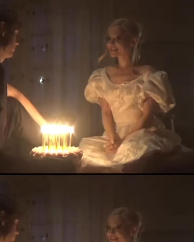 a woman sitting in front of a cake with lit candles