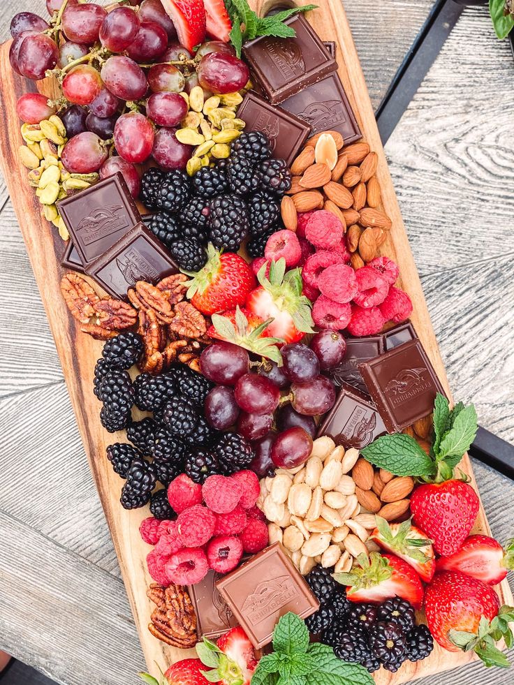 a wooden platter filled with assorted fruit and nuts