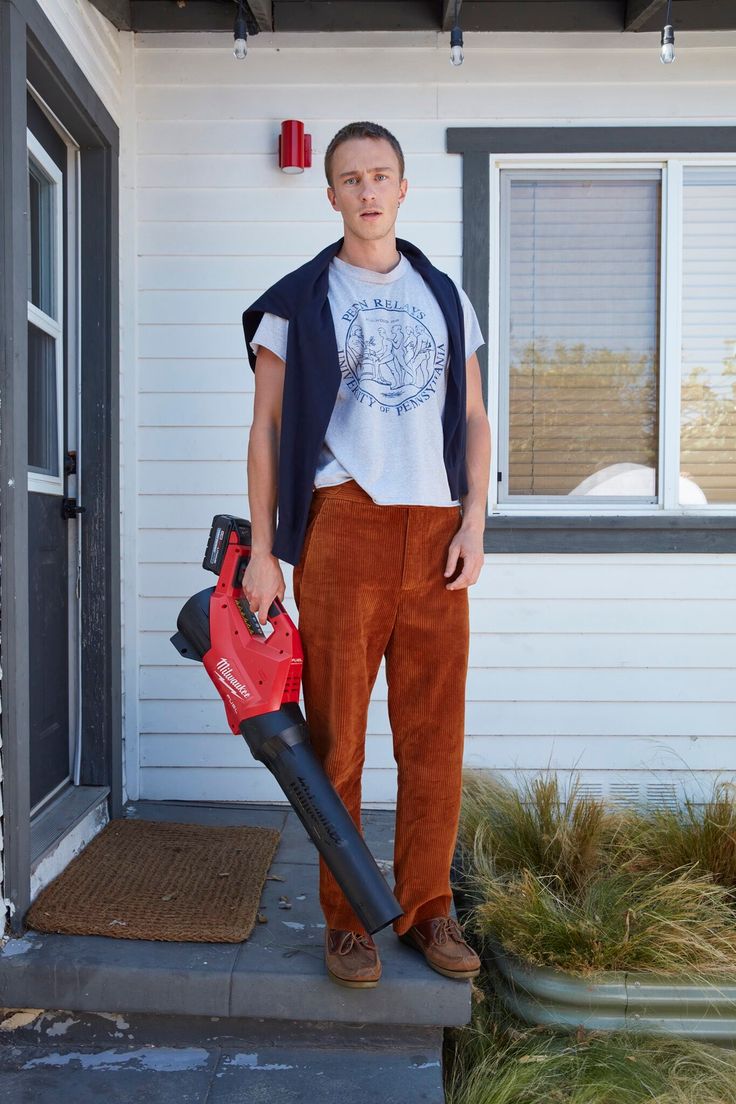 a man holding a red and black blow dryer in front of a white house