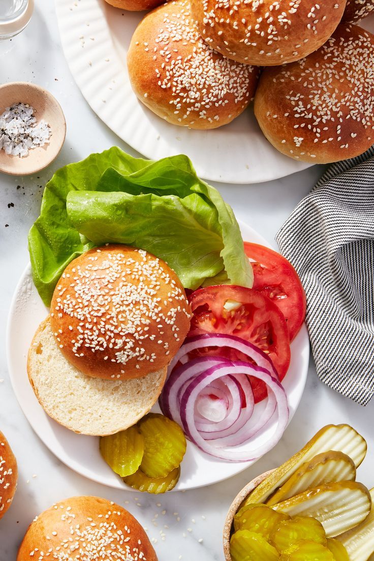 an assortment of burgers on plates with lettuce, tomato and onion slices