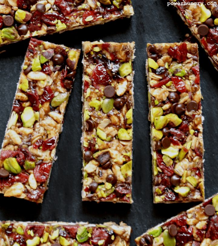 several pieces of fruit and nut bars on a black surface with nuts scattered around them