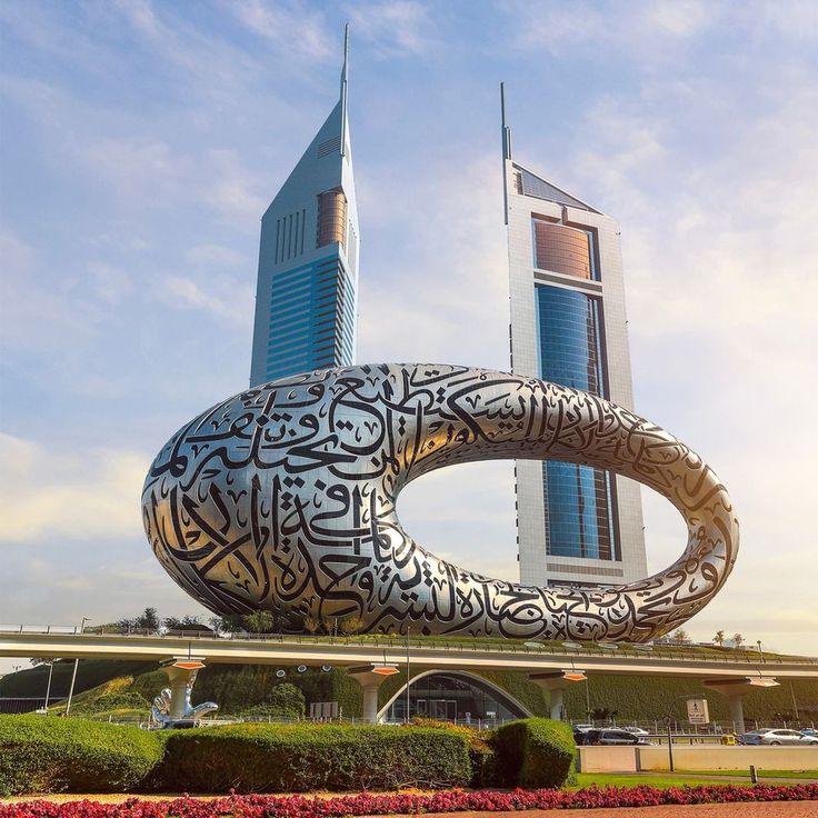 a large metal sculpture in front of a tall building with arabic writing on it's side