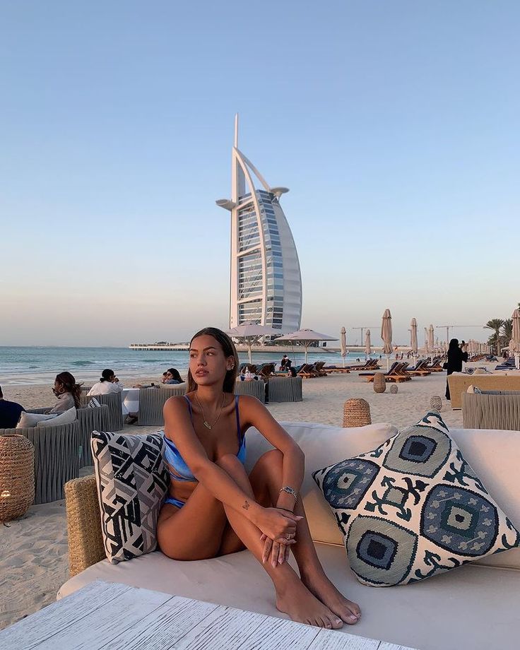 a woman sitting on top of a white couch next to the ocean in front of a tall building