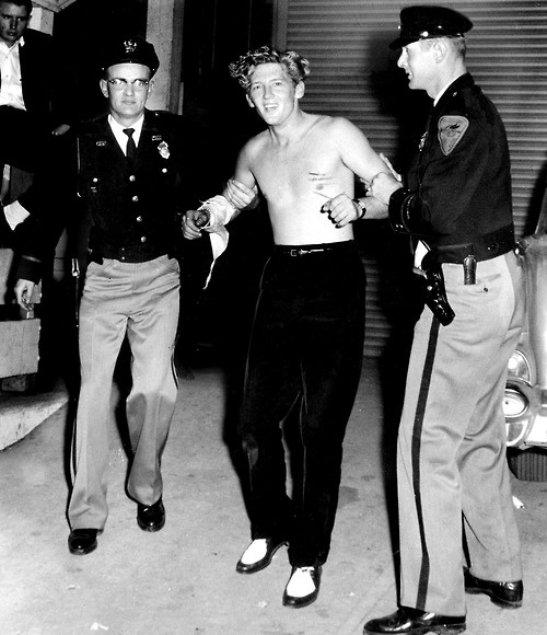 an old black and white photo of two men dancing with police officers in the background