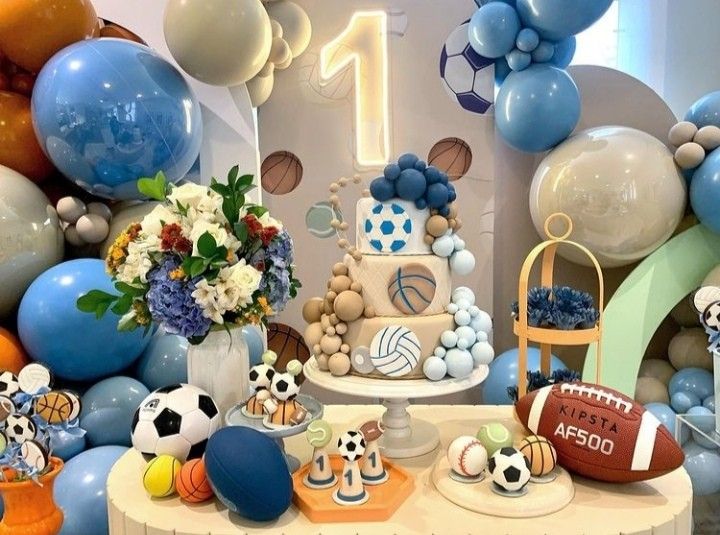 a table topped with balloons and cakes covered in blue, white and orange decorations for a sports themed birthday party