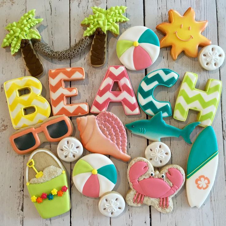 decorated cookies are laid out in the shape of letters and beach items on a white wooden surface